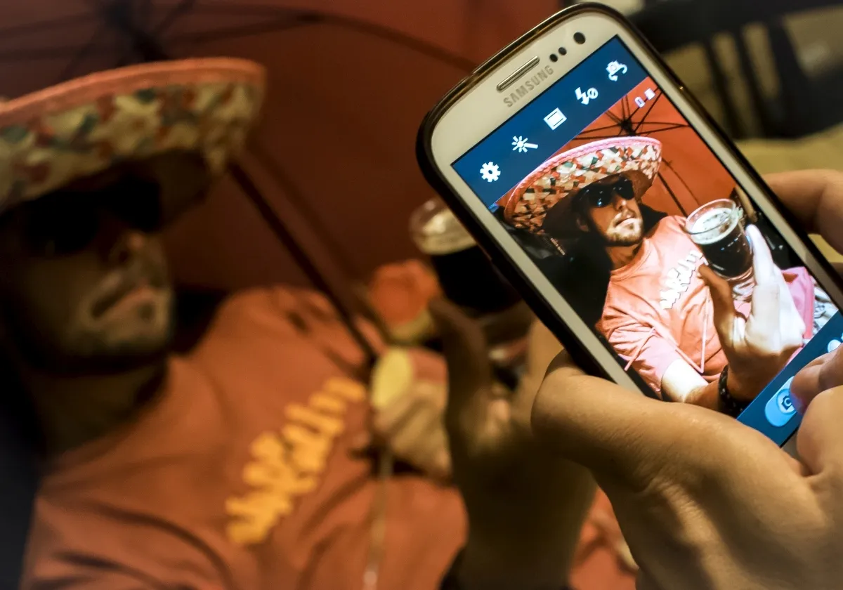 Smartphone screen photographing a man in a sombrero holding a drink